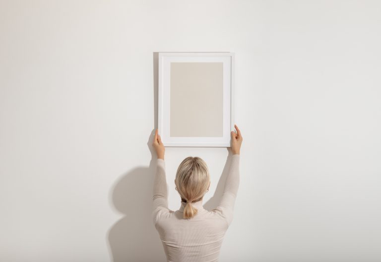 Woman hanging blank frame on wall representing building a real estate personal brand from the ground up